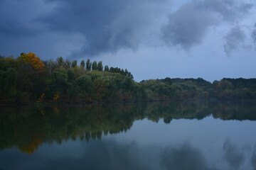 Obraz na płótnie Canvas The trees above the water in a light evening fog after a slight autumn rain.