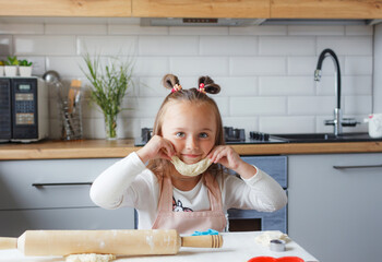 a cute little girl in an apron is sitting at the kitchen table and playing with the dough