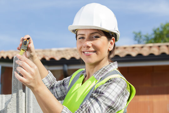 a happy female builder measuring outdoors
