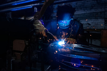 Side view of welder in protective helmet welding metal detail with sparks at factory