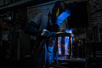Fototapeta na wymiar Side view of welder in protective helmet welding metal detail with sparks at factory