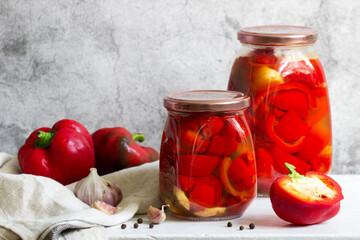 Pickled sweet peppers in glass jars on a light surface.