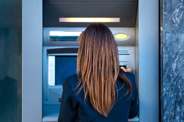 Fototapeta na wymiar Woman using an ATM machine. Withdrawing cash money from credit card at bank machine.