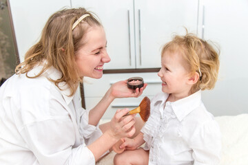 Portrait of woman doing makeup to her daughter in the bedroom on the bed