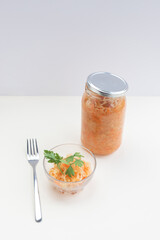 a jar with fermented cabbage, some salad on the plate and spices on a light background