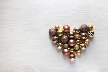 on a light wooden background beautiful glass balls of gold and pastel colors for decorating a Christmas tree lie in the form of a heart