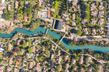 Aerial pass over Kibbutz Nir David with Asi river channel turquoise water dividing east and west side riverside houses and palm trees, Israel.