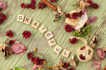 Flat lay image featuring border of various dried flowers surrounding wooden letters spelling the word grateful
