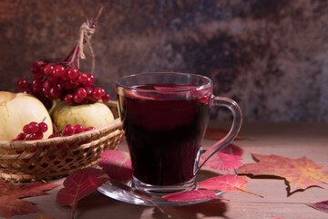 Drink mulled wine in a glass Cup on a dark wooden background with autumn leaves, viburnum berries and apples in a wicker vase. Horizontal orientation
