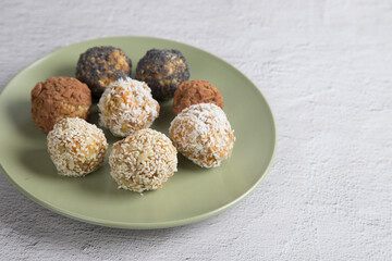 Homemade energy balls with dried fruits , nuts, sesame seeds, cocoa, almonds and poppy seeds on a plate on a light background. Vegan and vegetarian raw appetizer or food. Close-up, copy of the space.