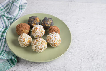 Homemade energy balls with dried fruits , nuts, sesame seeds, cocoa, almonds and poppy seeds on a plate, light background, green napkin. Vegan raw appetizer or food. Close-up, copy of the space.