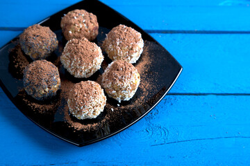 Homemade energy balls made of dried fruits, nuts, granola , sprinkled with cocoa on a black plate, blue wooden background . Vegan food. Close-up, copy space
