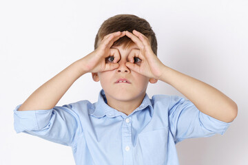 The boy expresses emotions, looks through his hands, like through binoculars. Isolated on white background.