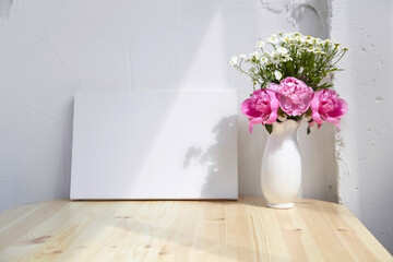 Mockup, blank canvas, vase with pink flowers on wooden table, white wall with shadows