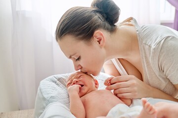 Obraz na płótnie Canvas Young mom kissing crying newborn baby son