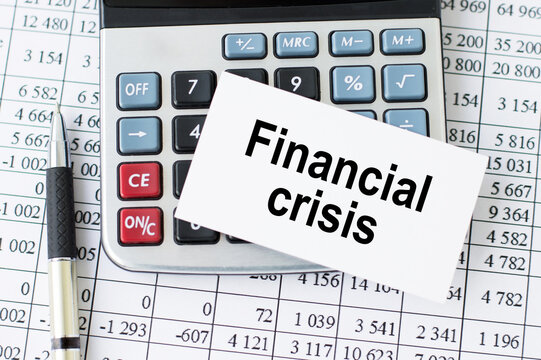 Financial crisis word written on a card lying on a calculator near a pen and financial reports