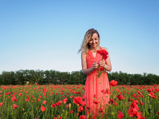 Obraz na płótnie Canvas Young girl in a red dress in a poppy field 