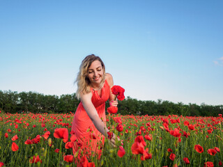 Naklejka na ściany i meble Young girl in a red dress in a poppy field 