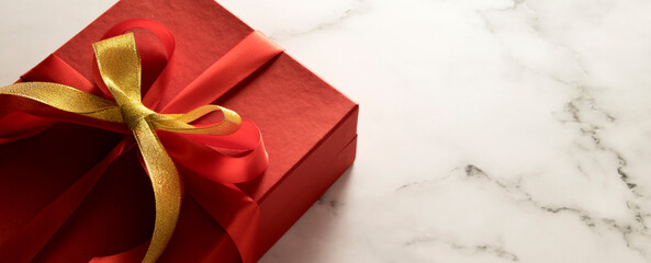 Red gift box with bow on marble table with copy space in banner format