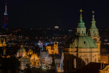 Fototapeta na wymiar The tower of the Church of St. Nicholas is a Baroque church located in Prague from 1625 in the center of Prague. in the background a view of street lights in the city at night