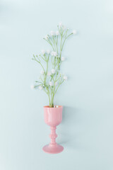 Creative spring concept made with  nature plant wild flowers decoration and  pink glass  on blue pastel minimal  background  Flat lay, top view