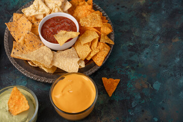 close-up view of plate with mexican nachos with guacamole, salsa and cheese dip on dark blue background. Traditional recipe. Tasty food concept.