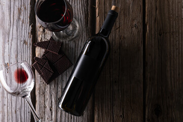 Top view of elegant bottle and wineglasses with red wine and dark chocolate on rustic wooden...
