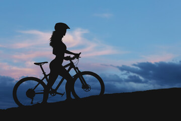Girl on a mountain bike on offroad, beautiful portrait of a cyclist at sunset, Fitness girl rides a modern carbon fiber mountain bike in sportswear.
