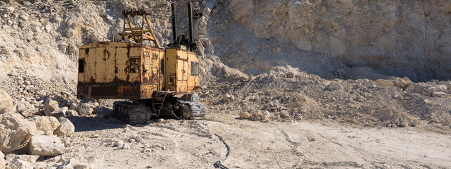A large yellow tracked excavator is mining rock in a quarry.