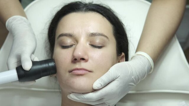 Young woman having facial microcurrent treatment in beauty salon. Beautician using electrical impulses for facial procedure to help serum absorb deep in skin. Healthcare, wellness and medicine