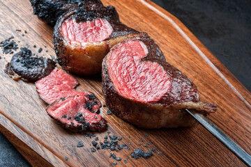 Modern style barbecue dry aged wagyu Brazilian picanha from the sirloin cap of rump beef sliced and offered as close-up on a skewer on a wooden design board on rustic black background