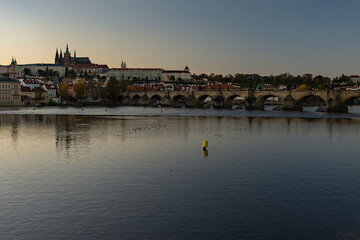view of the Vltava river and Prague Castle St. Vitus Cathedral and Charles Bridge in the center of Prague at sunset. there are reflections on the river surface and the sky is illuminated by the sun