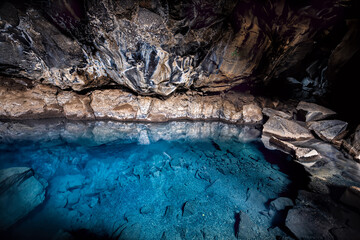 Inside of dark Grjotagja lava cave near lake Myvatn with hot springs blue water and rocks, rocky formations on walls reflection