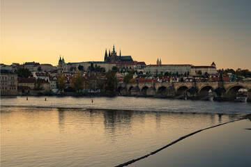 Fototapeta premium view of the Vltava river and Prague Castle St. Vitus Cathedral and Charles Bridge in the center of Prague at sunset. there are reflections on the river surface and the sky is illuminated by the sun
