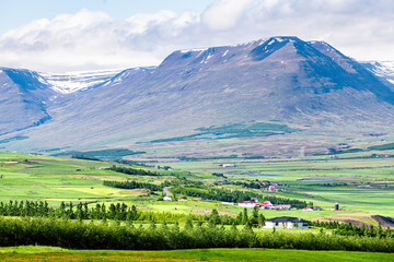 View of Sulur mountains near Akureyri with blue sky clouds and pasture farm pastoral landscape with green grass during summer day