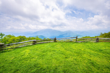 Devil's Knob Overlook with wooden fence and green grass field meadow at Wintergreen resort town village in Blue Ridge mountains in summer clouds mist fog
