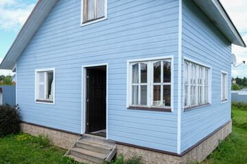 Fototapeta na wymiar White windows of a small tiny frame house with blue walls,a country residence in sunny summer day