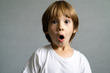 a small boy with the emotion of surprise on a light gray background in a white t shirt
