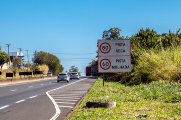 Signpost indicating "speed limit on dry and wet roads" in portuguese,on  Highway, SP 294, near the entrance of Marilia city