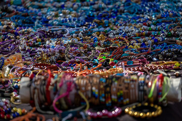 Fototapeta premium A table of decorative colorful cosmetic beads of luxury objects. The glamour balls, plastic jewelry, fashionable necklaces, and bracelets at a bazaar. The trinkets are of multiple colors.