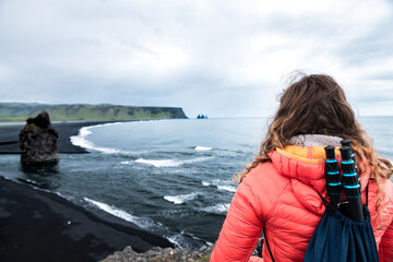 Fototapeta na wymiar Myrdal, Iceland Reynisfjara black sand beach and woman back closeup looking at volcanic rocky cliff formations with seashore coastline and waves crashing