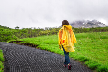 Skaftafell, Iceland green summer landscape and woman in yellow poncho walking hiking on wet trail...