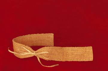 Burlap ribbon with gold tie on red background. Text message space at top. Christmas and holiday theme.