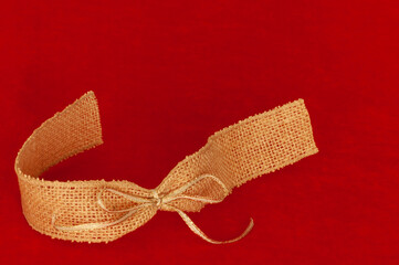 Fototapeta premium Ribbon at lower right corner framing text message space at top and right. Red background with burlap and gold ribbon bow in swirl curve shape.