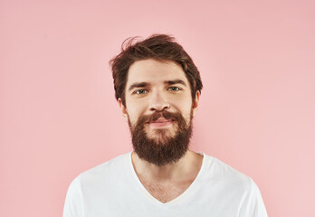 Fototapeta premium Portrait of a young man with a beard in a white T-shirt on a pink background