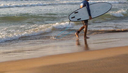 Surfer walking with surfboard on the beach. Summer time and active rest concept.
