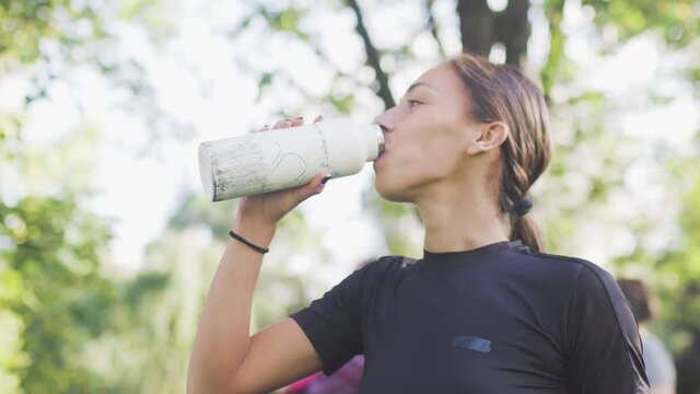 Fitness girl in tha park drinking and spilling water frоm a bidon