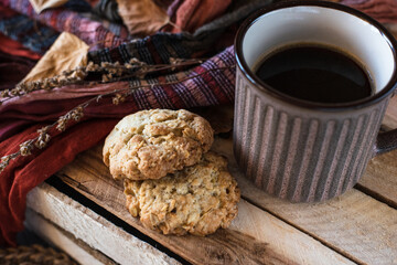 Oatmeal cookies with a mug of black coffee on a wooden box with dried flowers, an orange-brown scarf