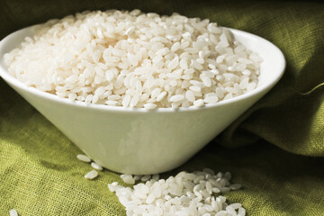 A porcelain bowl with white rice and oatmeal is on the kitchen table, with a light green tablecloth in the background.