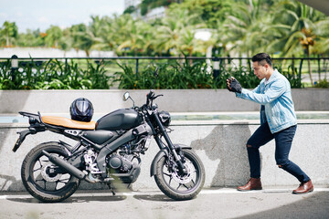 Fototapeta na wymiar Handsome young Asian man taking photo of his motorcycle on smartphone